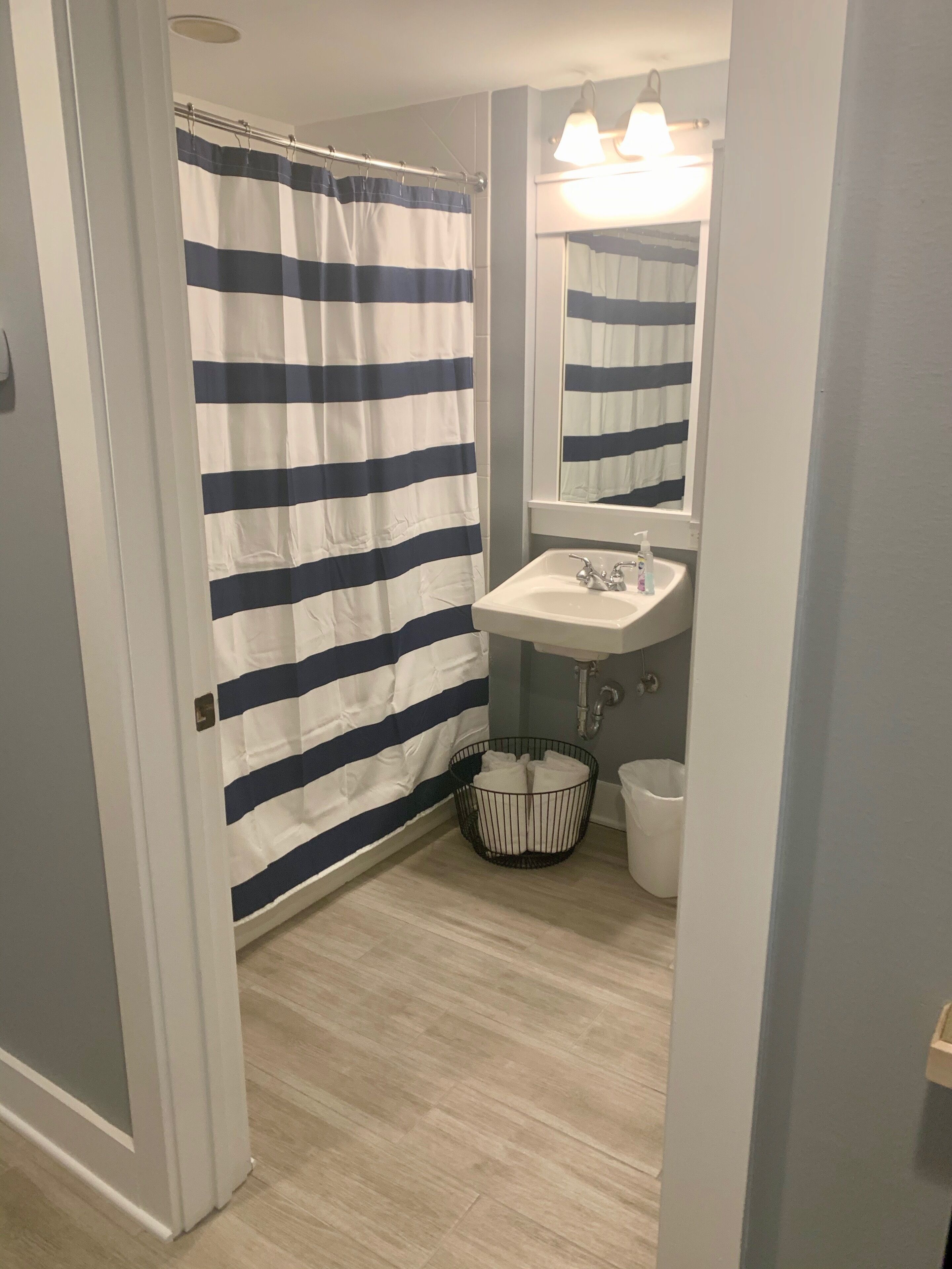 A bathroom with a striped shower curtain, a sink, a mirror, and a waste basket.