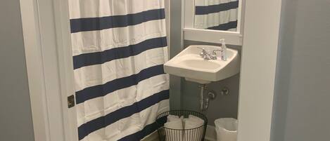 A bathroom with a striped shower curtain, a sink, a mirror, and a waste basket.