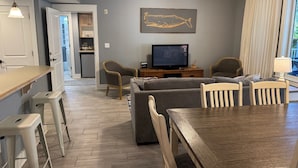 Una sala de estar con televisor, ventilador de techo, mesa de comedor y una cocina al fondo.