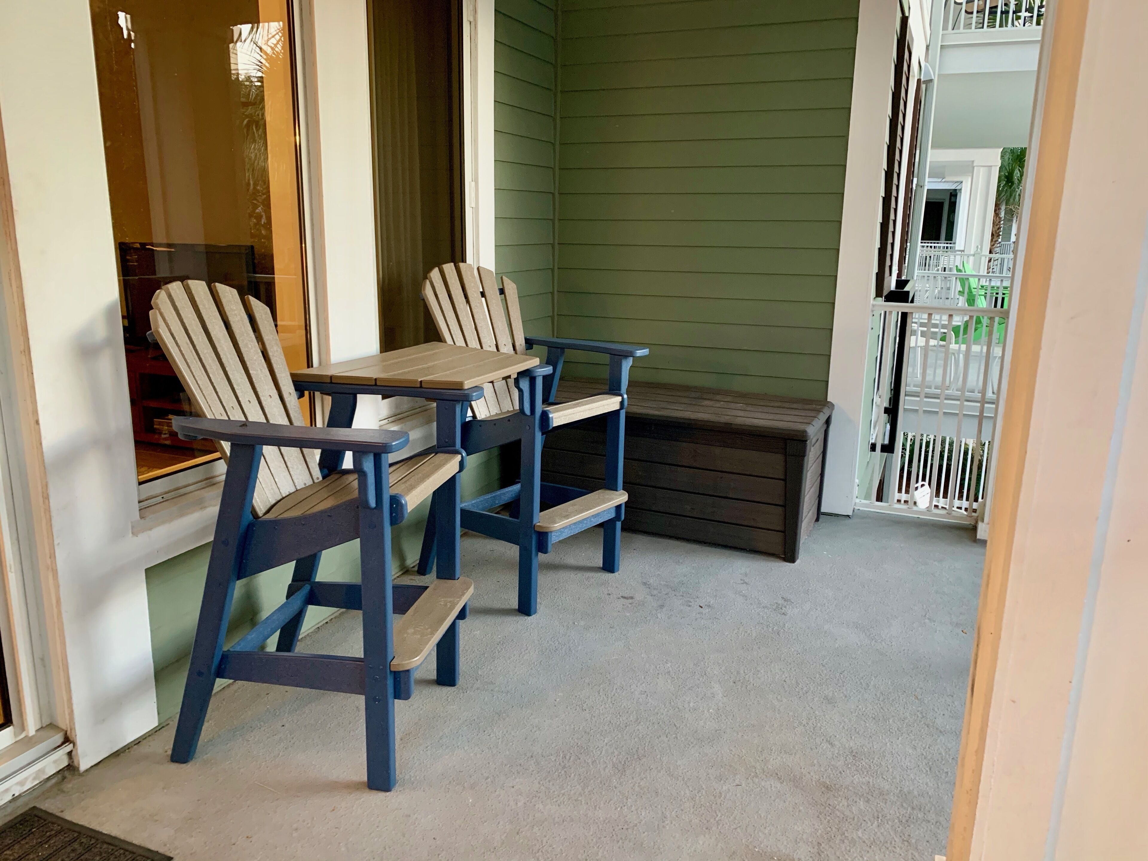 A small outdoor seating area with two Adirondack chairs and a wooden table.