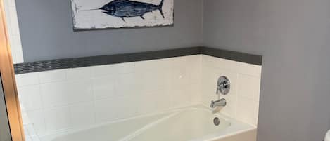 A bathroom with a bathtub, two wall-mounted fish paintings, a toilet, and a shower area.