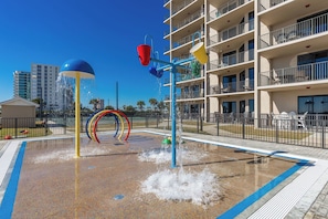 Un espace de jeux aquatiques avec une piscine, un bâtiment à plusieurs étages et un ciel d’un bleu limpide.