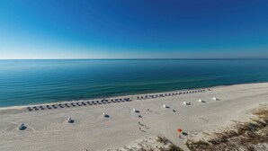 Une plage bordée de rangées de parasols et de chaises longues, un ciel dégagé et une mer calme.