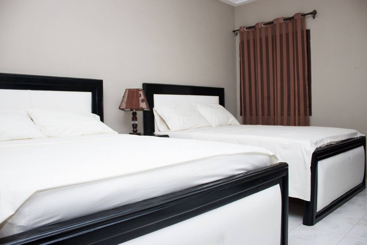 Een hotelkamer met twee bedden, een nachtkastje met een lamp en een raam met gordijnen.