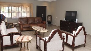 Uma sala de estar com um sofá de couro marrom, uma mesa de centro de madeira e uma TV sobre um armário de madeira escura.