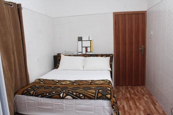 A small, neatly arranged bedroom with a bed, a wooden door, and a wall-mounted artwork. - Rose Leat Elegant Bed & Breakfast (Accra)