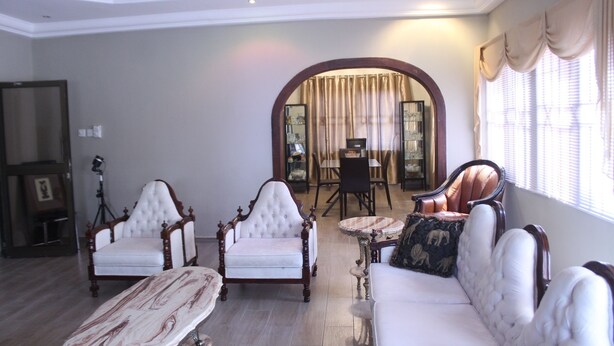 Uma sala de estar ampla com teto alto, móveis elegantes e uma grande porta em arco que dá para outro cômodo.