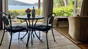 A room with a round table, two chairs, a bottle of wine, and a glass. There is a view of a lake and greenery outside. - Maple Bay beachfront suite, just steps to your private beach patio (Duncan)