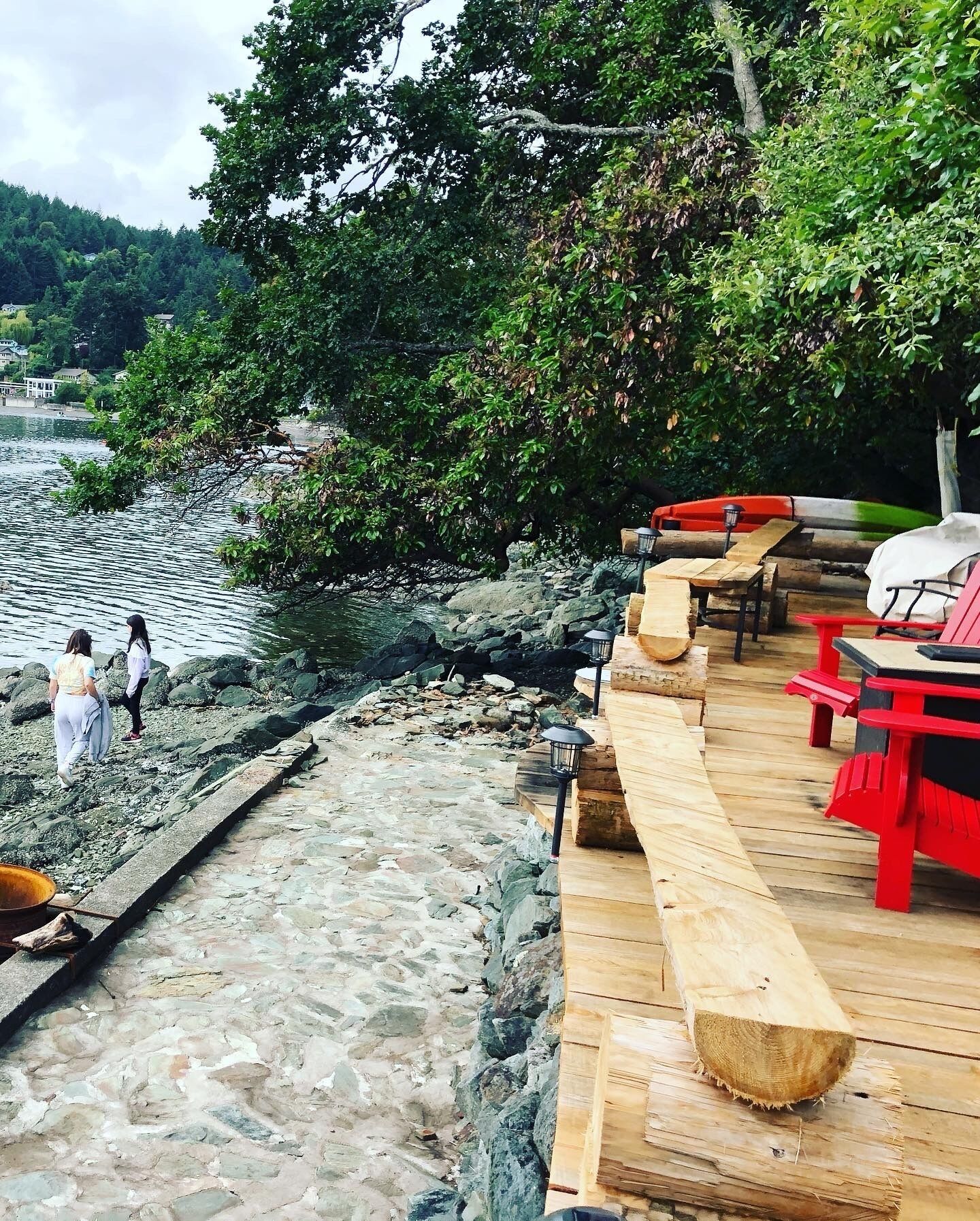 A wooden deck with picnic tables and a view of a rocky shoreline and calm water.