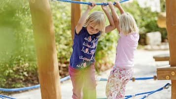 Two children playing on a rope bridge at an outdoor playground.
