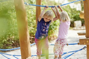 Dos niños jugando en un puente colgante en un parque infantil al aire libre.