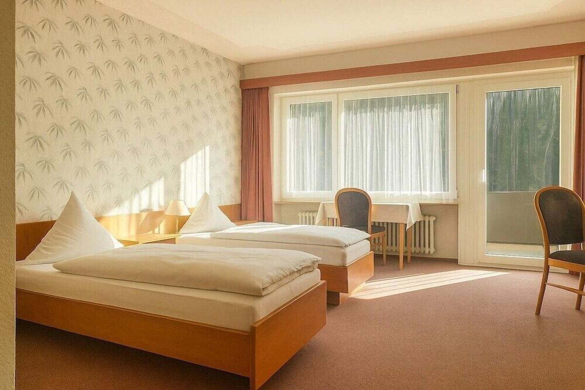 A hotel room with two beds, a desk, chairs, and a large window.