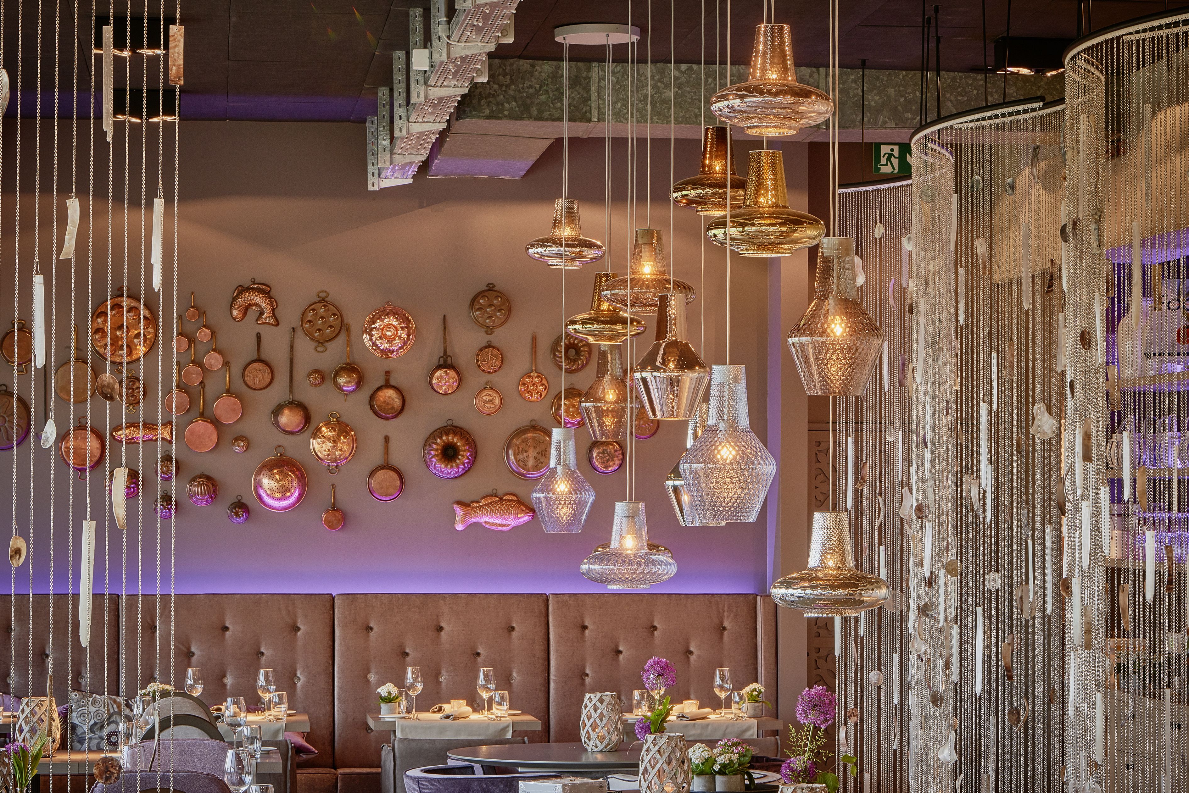 Interior de restaurante con lámparas colgantes, una pared decorada con platos y cuencos, y un área de mesas dispuestas para comer.