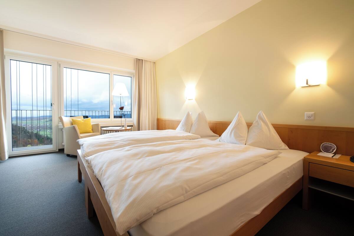 A hotel room with two beds, a balcony with a view, and a small table with a chair.