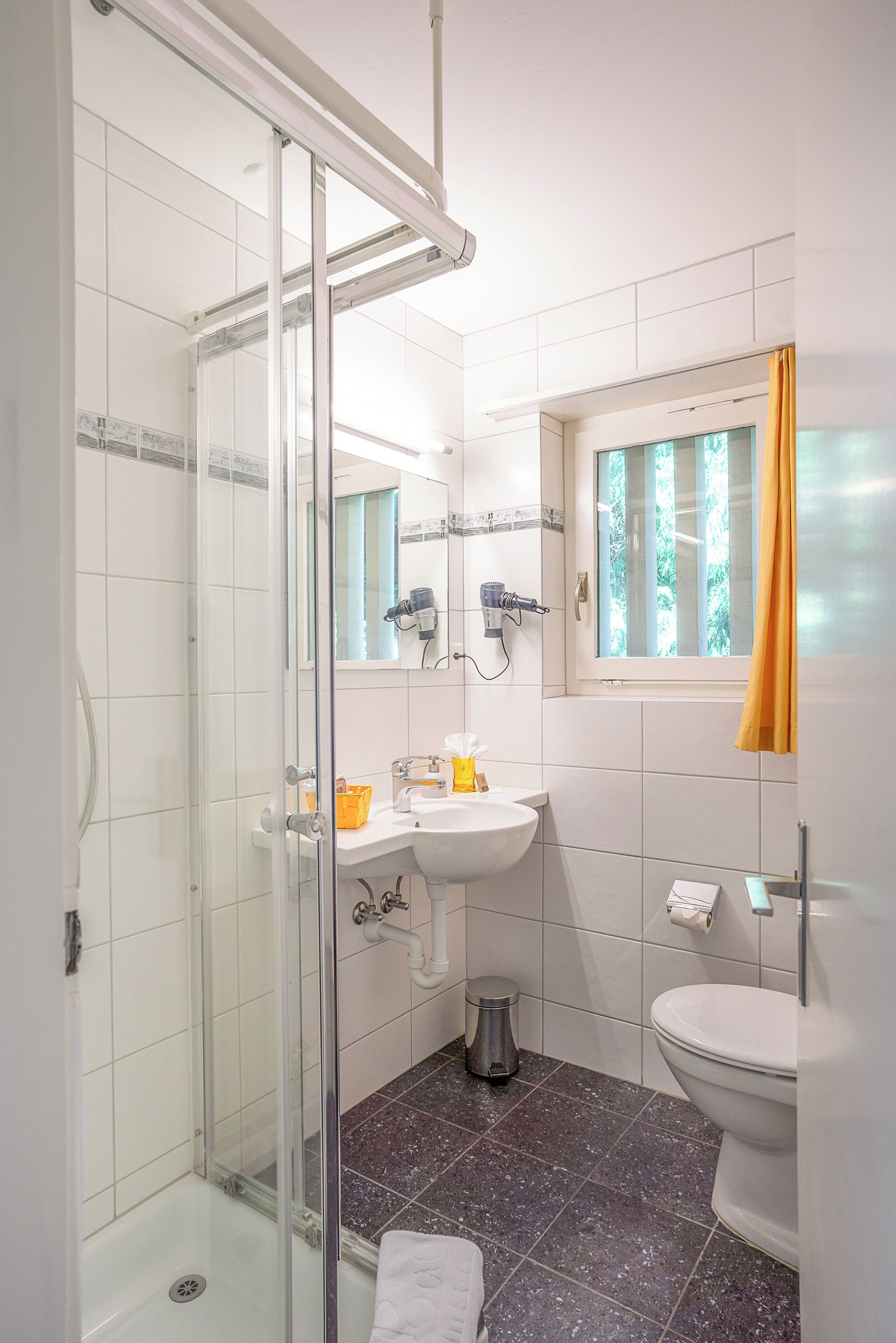 Un baño con cabina de ducha de vidrio, un lavabo, un inodoro y una ventana con cortinas.