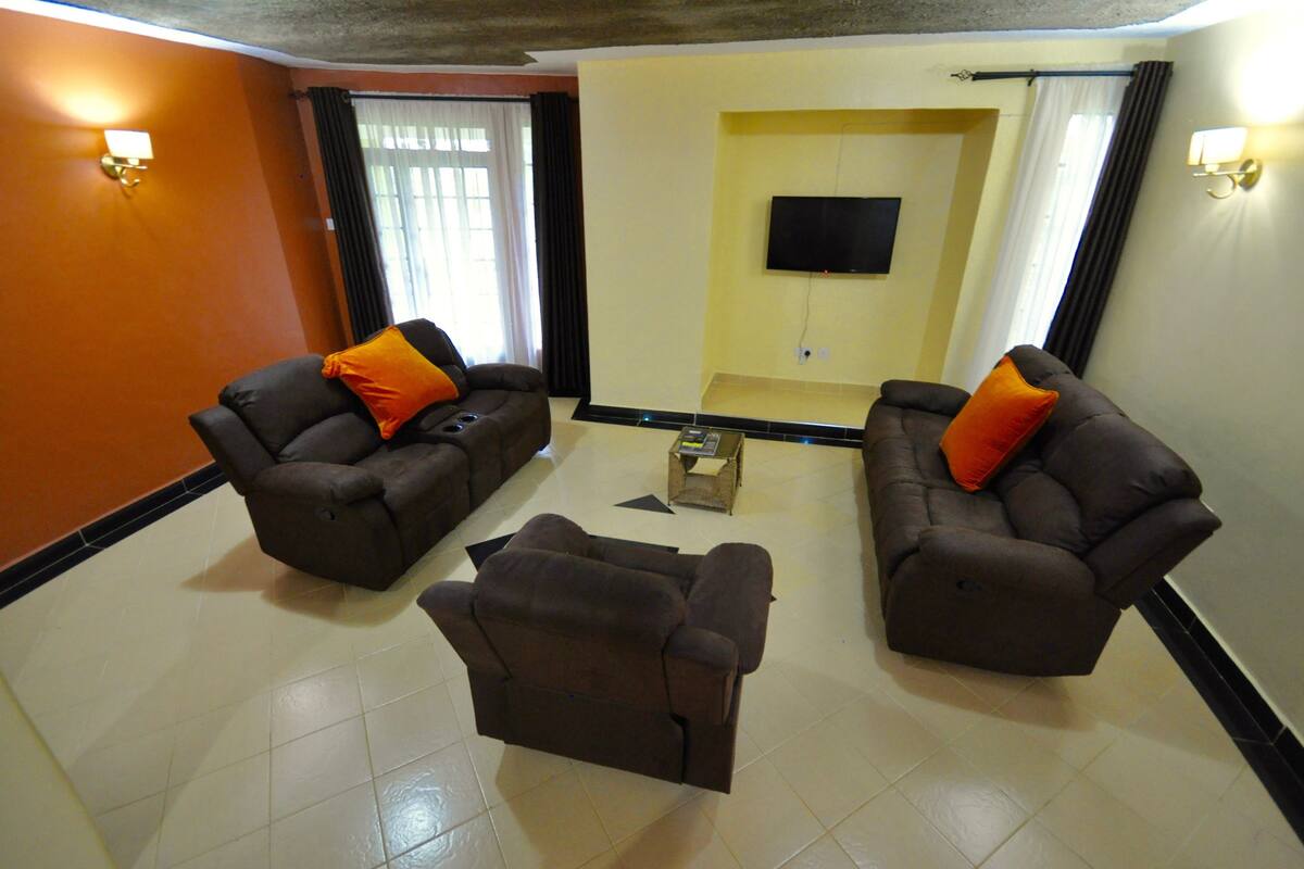 Una sala de estar con dos sofás, una mesa de centro, un televisor de pantalla plana montado en la pared y una ventana con cortinas.