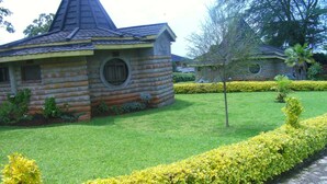 A log cabin with a conical roof and circular windows, surrounded by well-maintained grass and hedges. - Sosa Cottages (Gisambai)