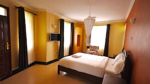 A hotel room with a bed, a chair, a television, and a window with curtains. - Sosa Cottages (Gisambai)