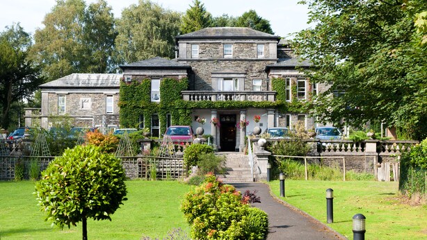 A stone building with a central entrance, surrounded by a well-maintained garden and a pathway leading to the entrance. - Windermere Manor Hotel (Windermere)