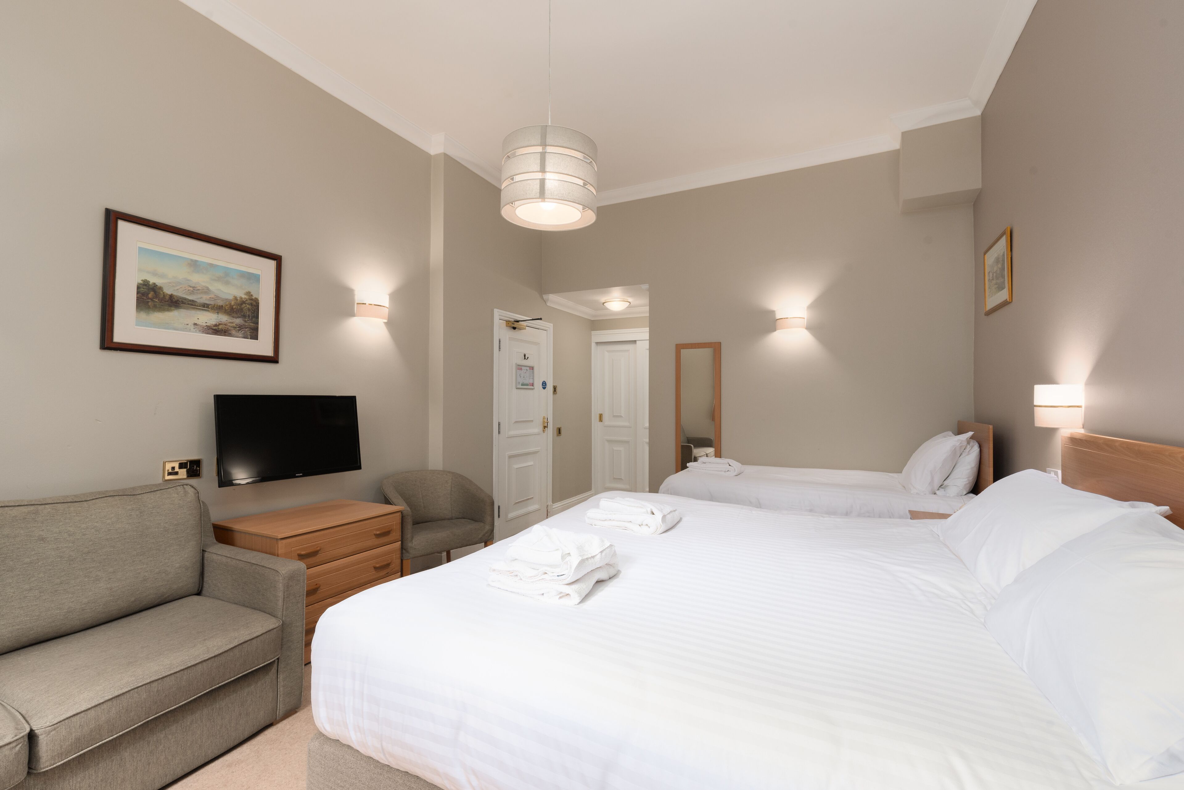 Una habitación de hotel con una cama, un sofá, un televisor y un cuadro en la pared.