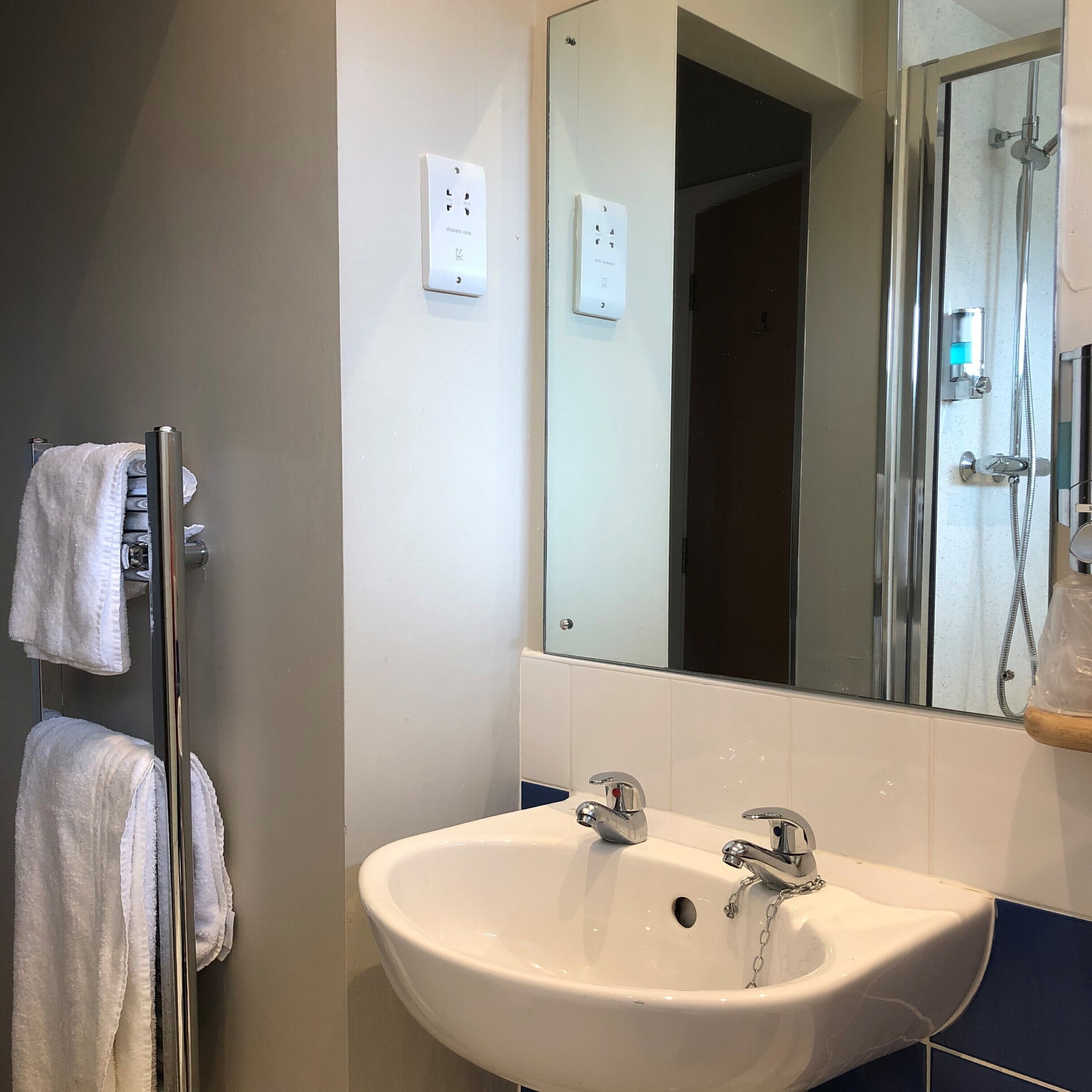 Un baño con lavamanos blanco, espejo y perchero para toallas.