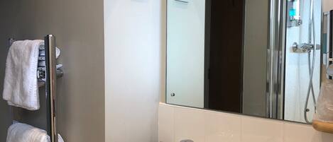 Un baño con lavamanos blanco, espejo y perchero para toallas.