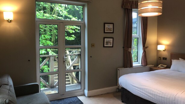 Ein Hotelzimmer mit einer großen Schiebeglasdoor zum Balkon, einem Bett mit weißer Bettwäsche, einem Nachttisch mit Lampe und einem an der Wand montierten Telefon.