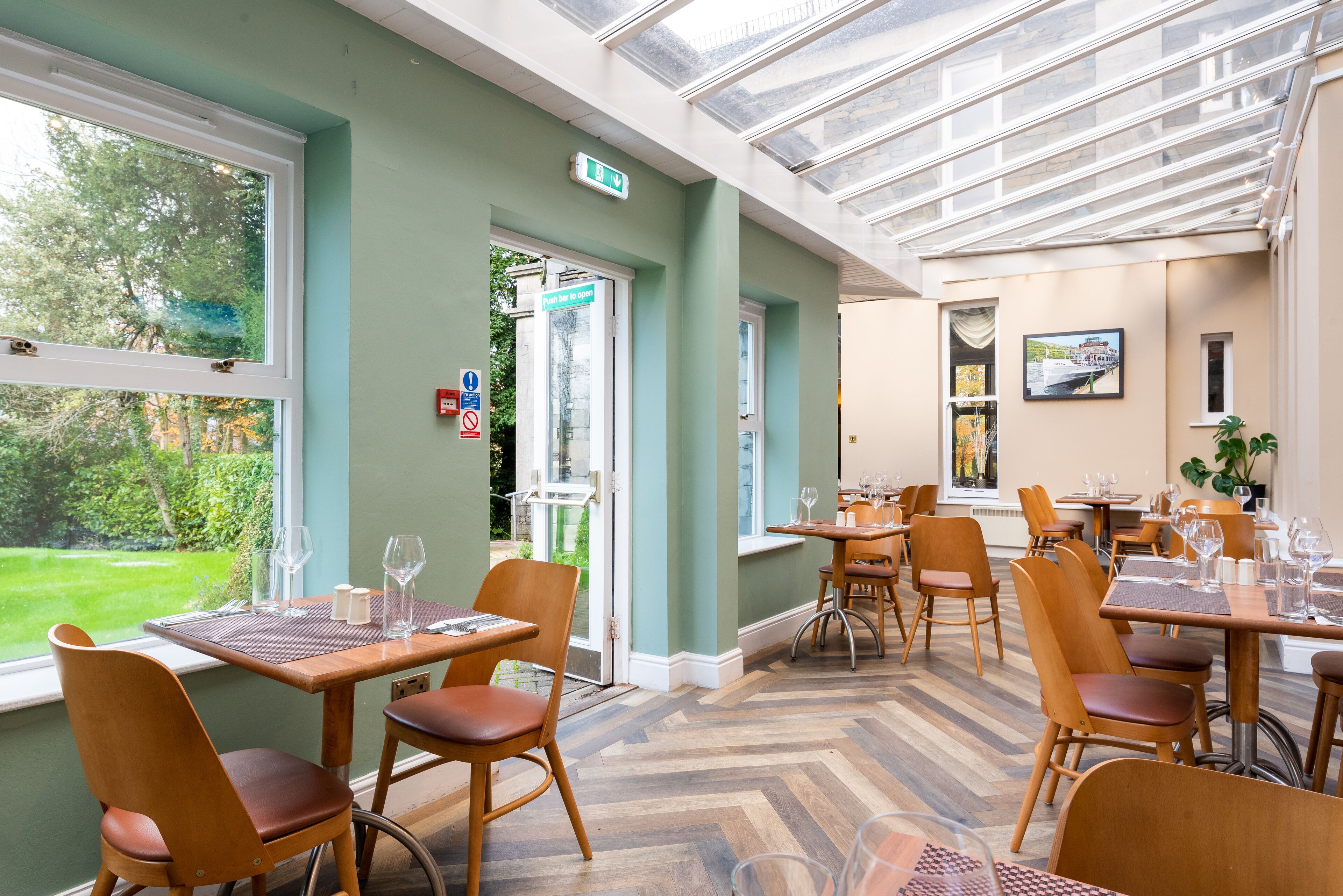 Ein Restaurant mit Holztischen und -stühlen, großen Fenstern und Blick ins Freie.