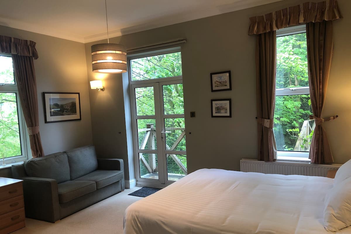 Quarto com cama, sofá, escrivaninha e janela com cortinas.