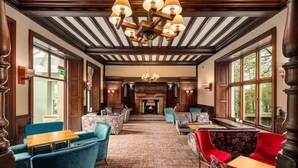 A hotel lobby with a fireplace, wooden ceiling beams, and seating areas. - Windermere Manor Hotel (Windermere)