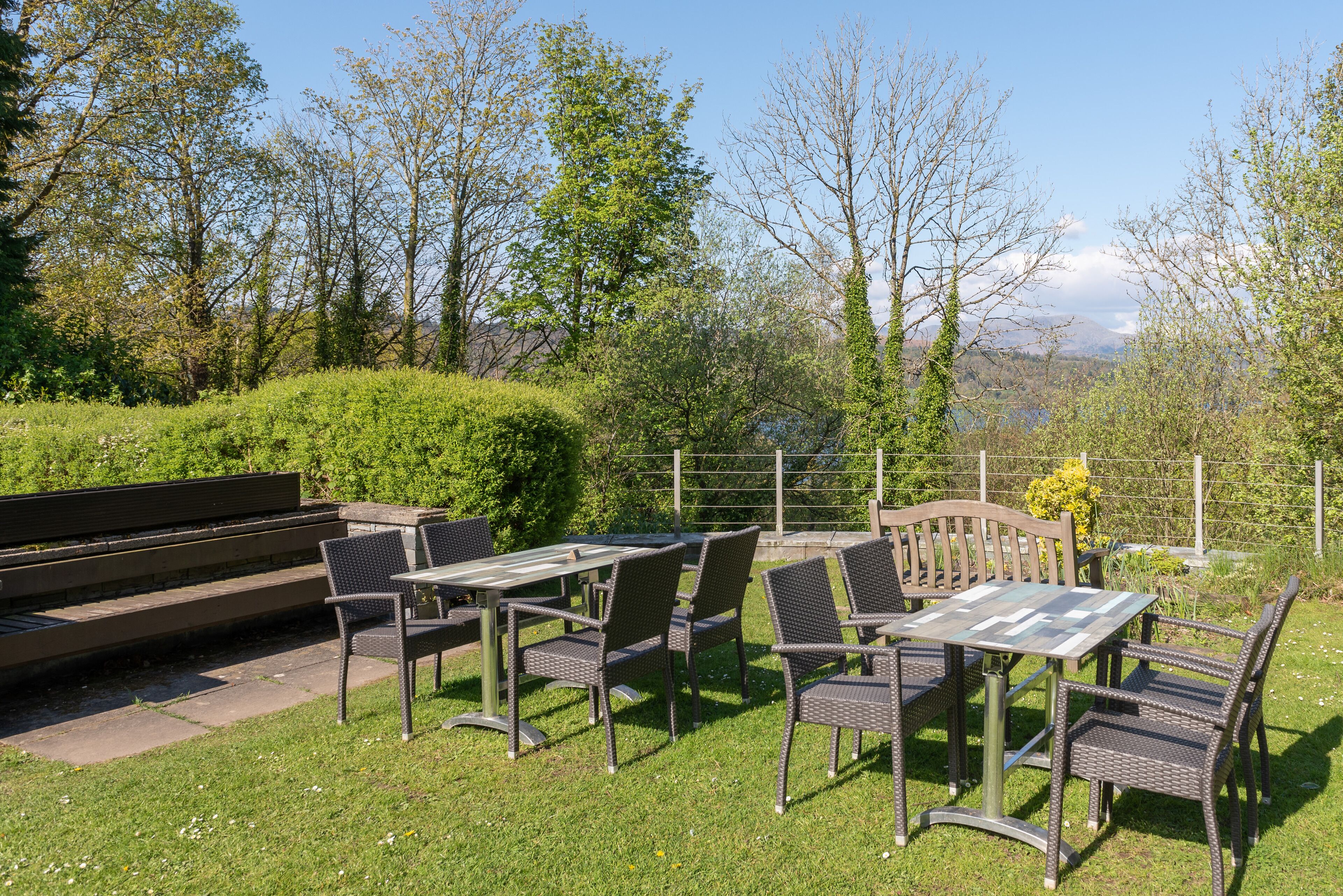 Un espace extérieur aménagé avec des chaises et une table en osier, entouré d’une pelouse bien entretenue et d’arbres.