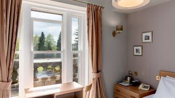 A bedroom with a desk, a bed, a bedside table with a phone, and a wall-mounted lamp.
