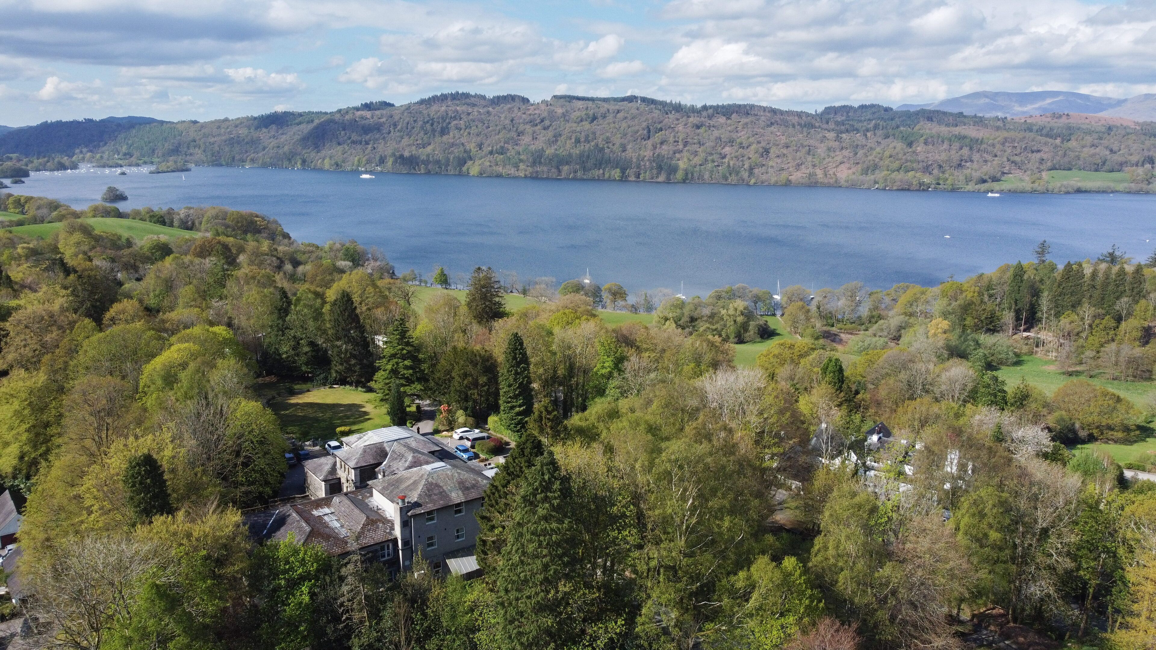 A residential area with houses surrounded by dense trees, a lake, and distant hills.