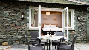 A stone-walled room with a bed, two wall-mounted lights, and a table with chairs. - Windermere Manor Hotel (Windermere)