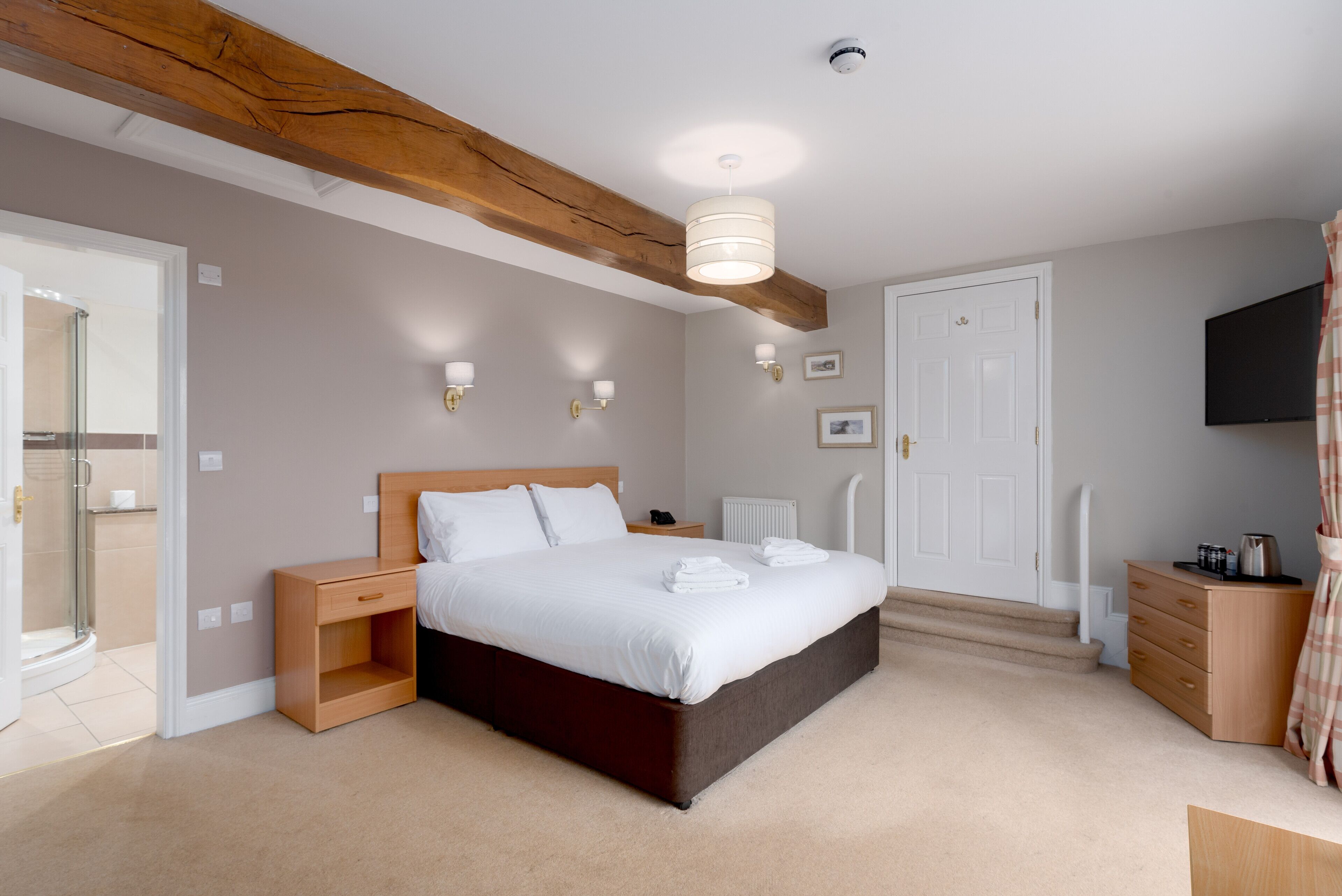 A bedroom with a large bed, bedside tables, a wardrobe, a shower, and a mounted TV.