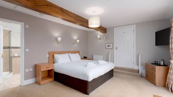A bedroom with a large bed, bedside tables, a wardrobe, a shower, and a mounted TV.