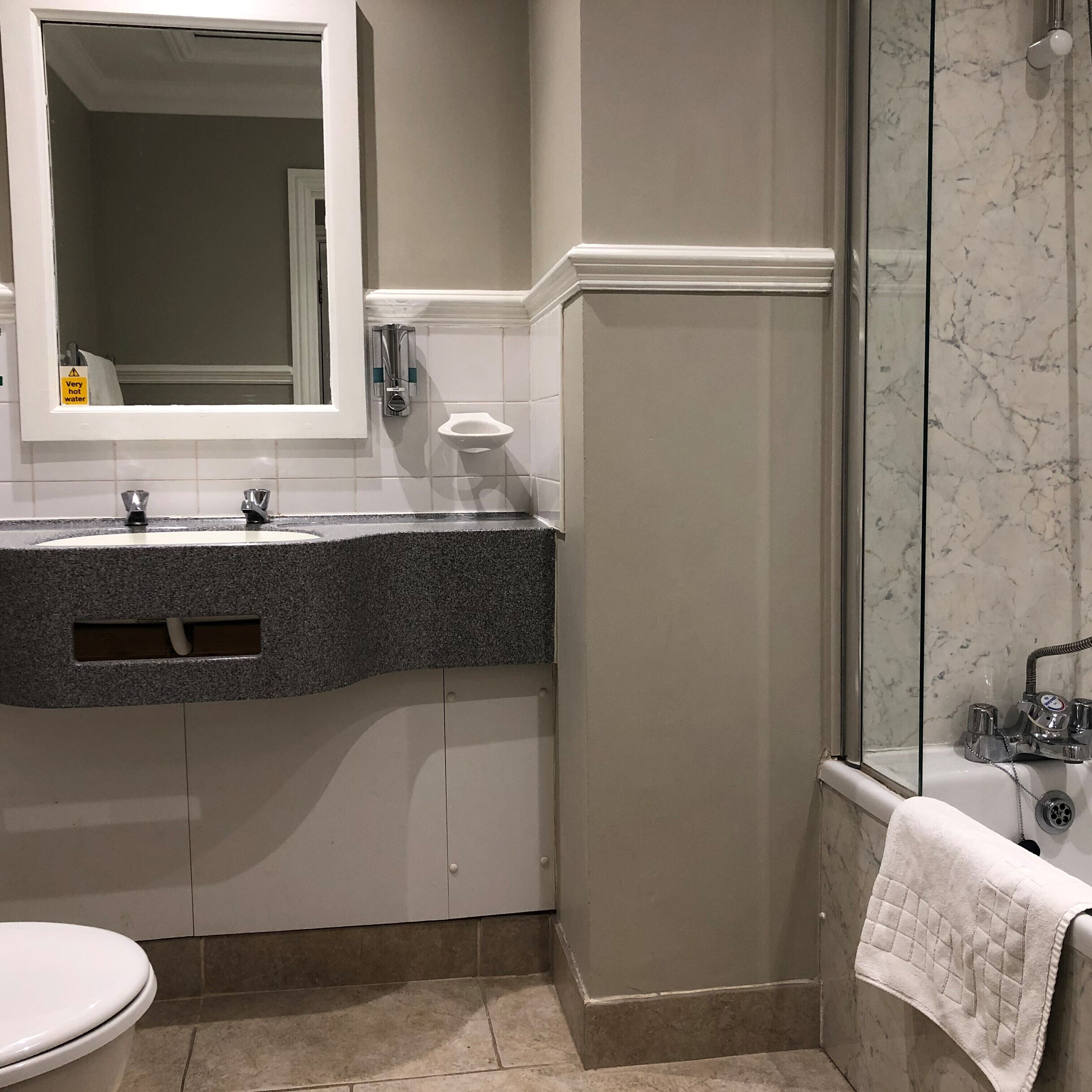 A bathroom with a marble shower, a toilet, and a sink with a mirror above it.