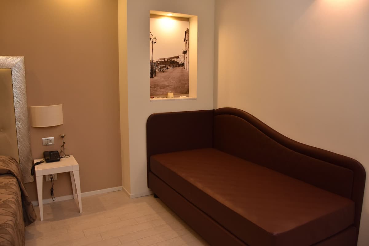 A bedroom with a brown sofa, a small bedside table with a lamp, and a framed picture on the wall.