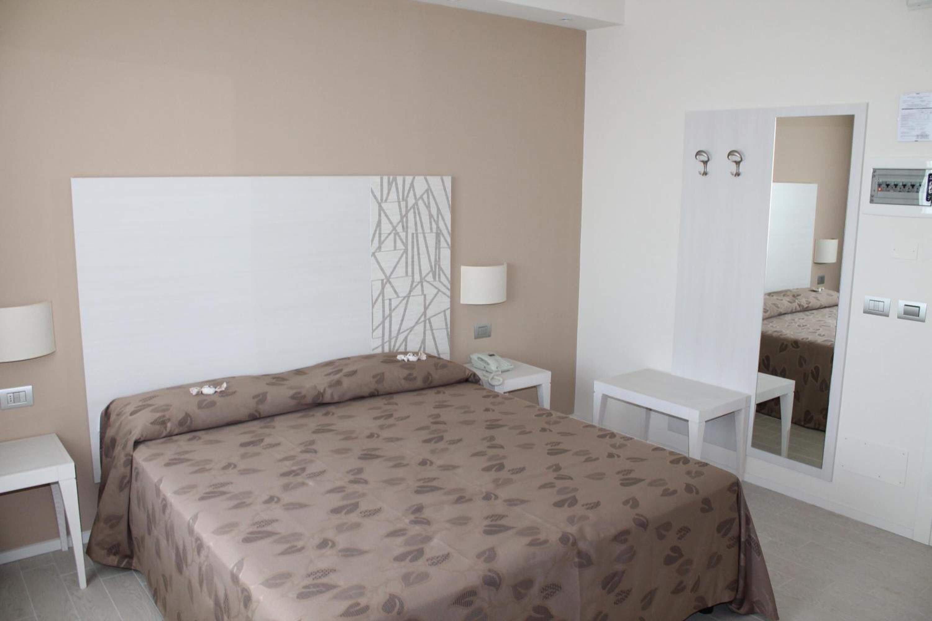 A hotel room with a bed, bedside tables, a mirror, and a wall-mounted control panel.