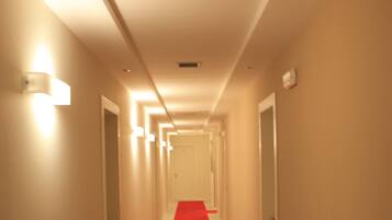 Un long couloir étroit, typique des hôtels, avec un tapis rouge, des murs blancs et des portes de part et d’autre.