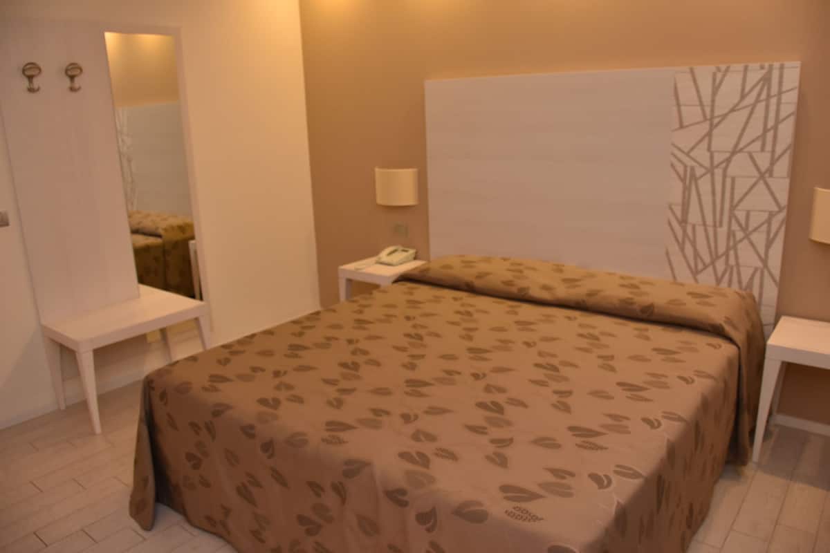 A bedroom with a bed, bedside tables, a mirror, and a wall with a geometric pattern.