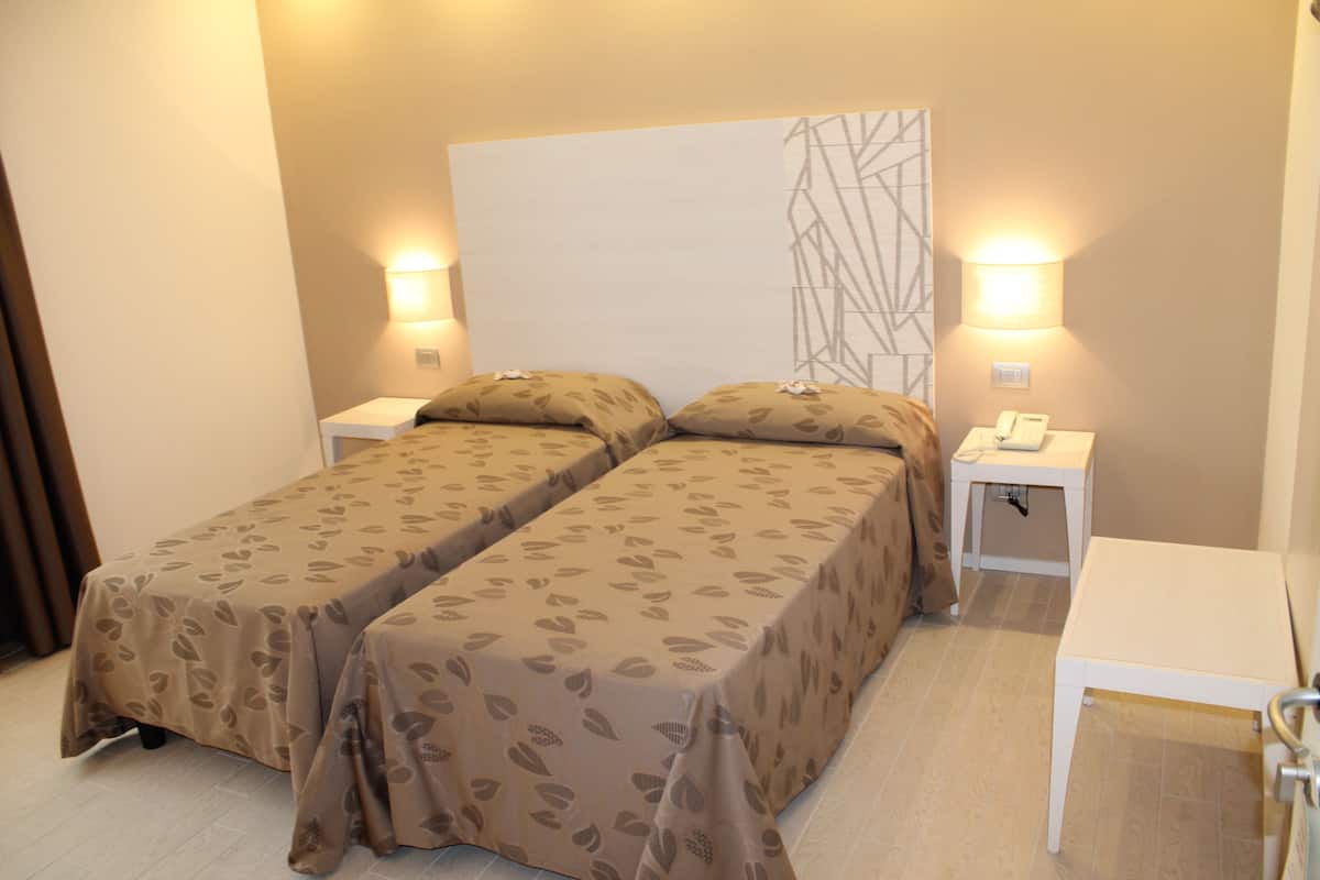 A double bed with a leaf-patterned bedspread, two bedside tables with lamps, and a wall-mounted light fixture.