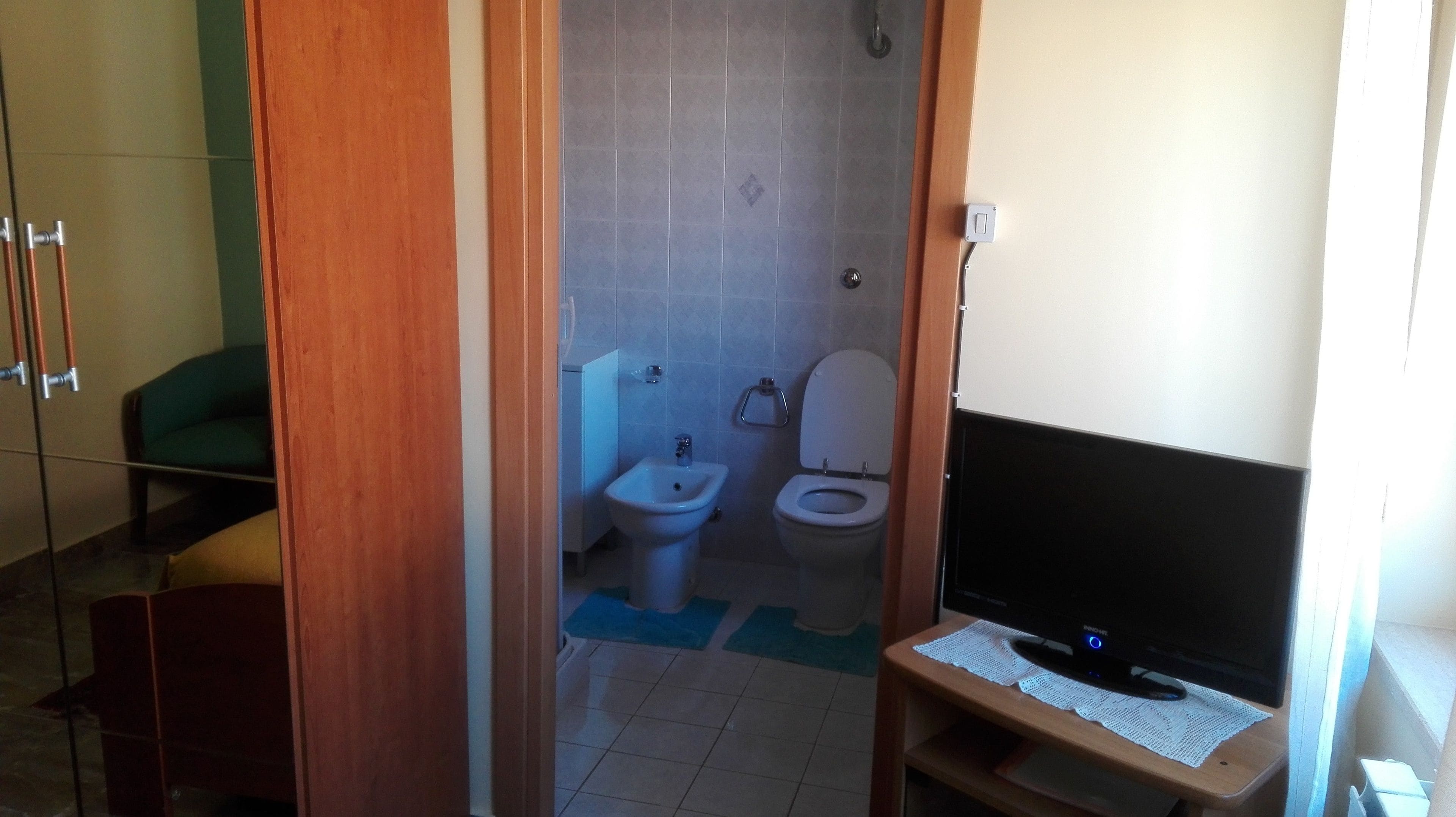 A small bathroom with a toilet, bidet, and a television on a wooden stand.
