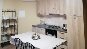 A compact kitchen with a gas stove, wooden cabinets, and a dining table with chairs. - B&B Agave (Reggio Calabria)