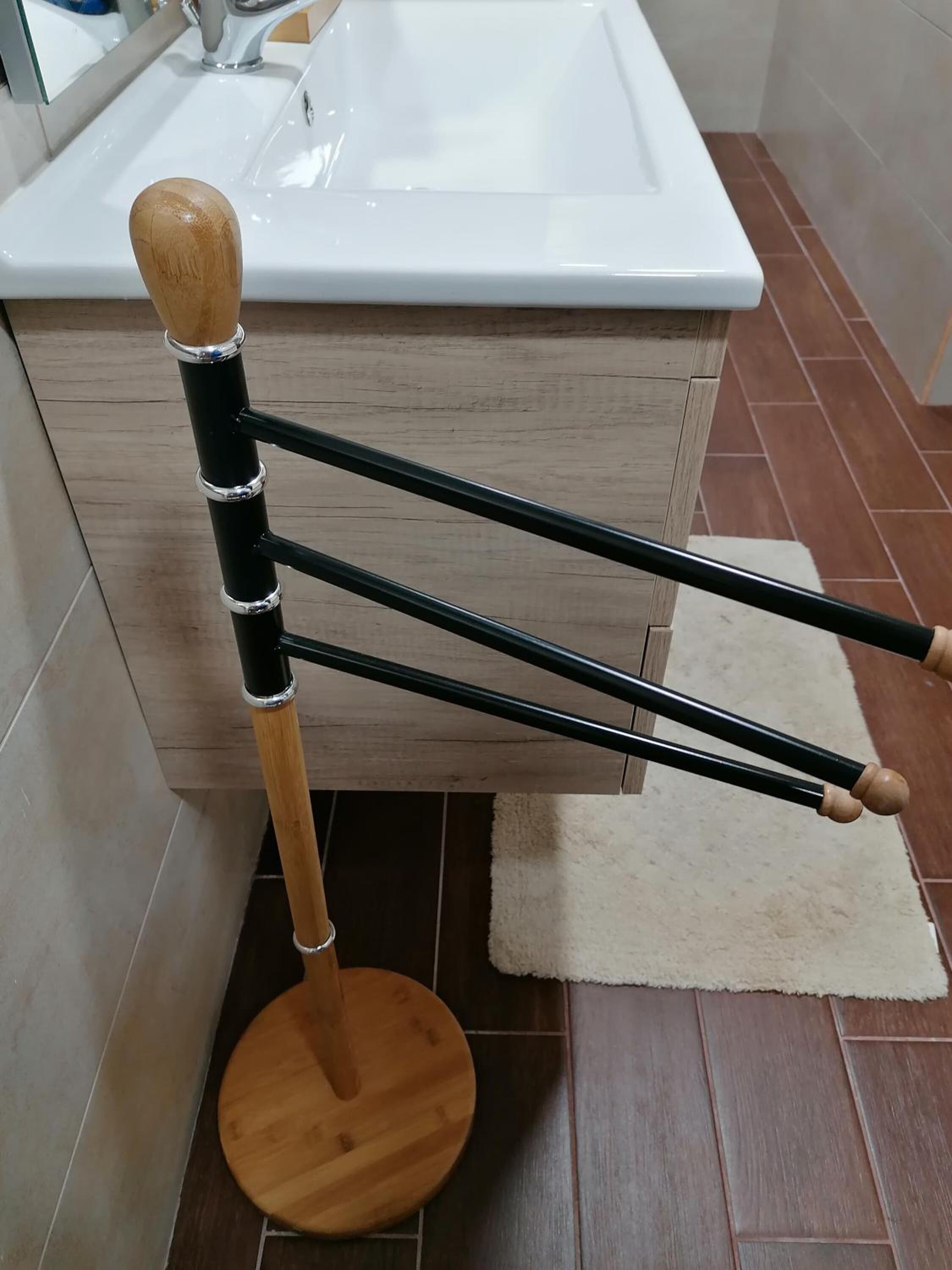 A wooden stool with a white top, positioned in front of a bathroom sink and cabinet.