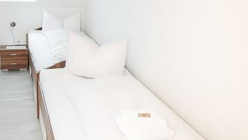 Hotellihuone, jossa on pitkä sänky, yöpöytä, ikkuna ja seinälle ripustettu taulu.