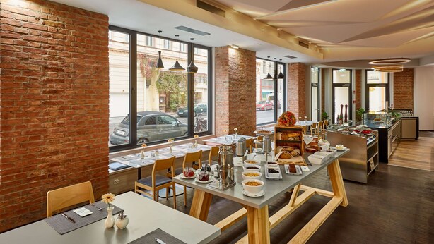 Un espace repas moderne avec des murs en briques, de grandes fenêtres et une variété d’aliments pour le petit-déjeuner disposés sur les tables.