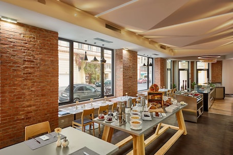 A modern dining area with brick walls, large windows, and a variety of breakfast items on tables.