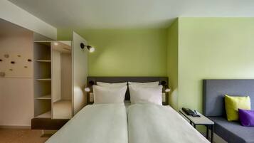 Een hotelkamer met een bed, nachtkastje en een bank met kussens.