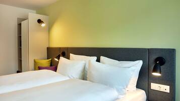 A neatly made bed with white and purple pillows, a grey headboard, and two wall-mounted lights.